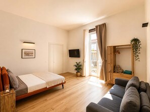 A bedroom with a bed, a sofa, a TV, a window with curtains, a door, and a small plant. - Dante Rooftop Hub: Vibrant Naples for 14 Guests (Naples)