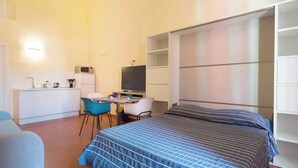 A compact room with a bed, a desk with a chair, a television, and a kitchenette. - Appartamento spazioso Napoli centro con terrazzo (Naples)