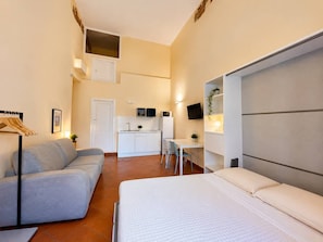 A compact hotel room with a bed, a sofa, a kitchenette, and a small dining area. - Appartamento spazioso Napoli centro con terrazzo (Naples)