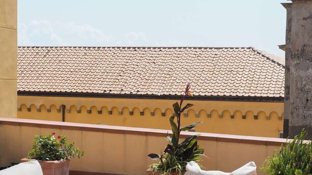 A rooftop terrace with white cushioned seating, a round table with glasses, and potted plants. - Appartamento spazioso Napoli centro con terrazzo (Naples)