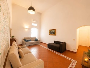 Uma sala de estar com um sofá, uma poltrona preta, um quadro na parede e um tapete estampado.