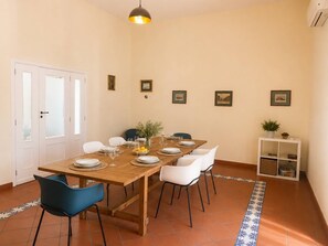 A dining area with a wooden table, white chairs, and a small potted plant on a white shelf. - Appartamento spazioso Napoli centro con terrazzo (Naples)