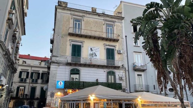 Vista de una calle con un edificio que tiene un balcón y un café con terraza.