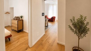 Un pasillo con suelo de madera, un sofá rojo, una mesa de comedor con sillas y una planta en maceta.