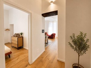 A hallway with a wooden floor, a red sofa, a dining table with chairs, and a potted plant. - Dante Sky Apt: Flowers Room & Terrace (Naples)