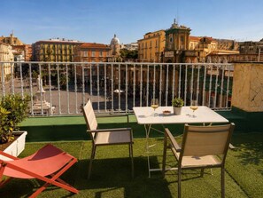 An outdoor terrace with a table and chairs, a view of the cityscape, and a railing. - Dante Sky Apt: Flowers Room & Terrace (Naples)