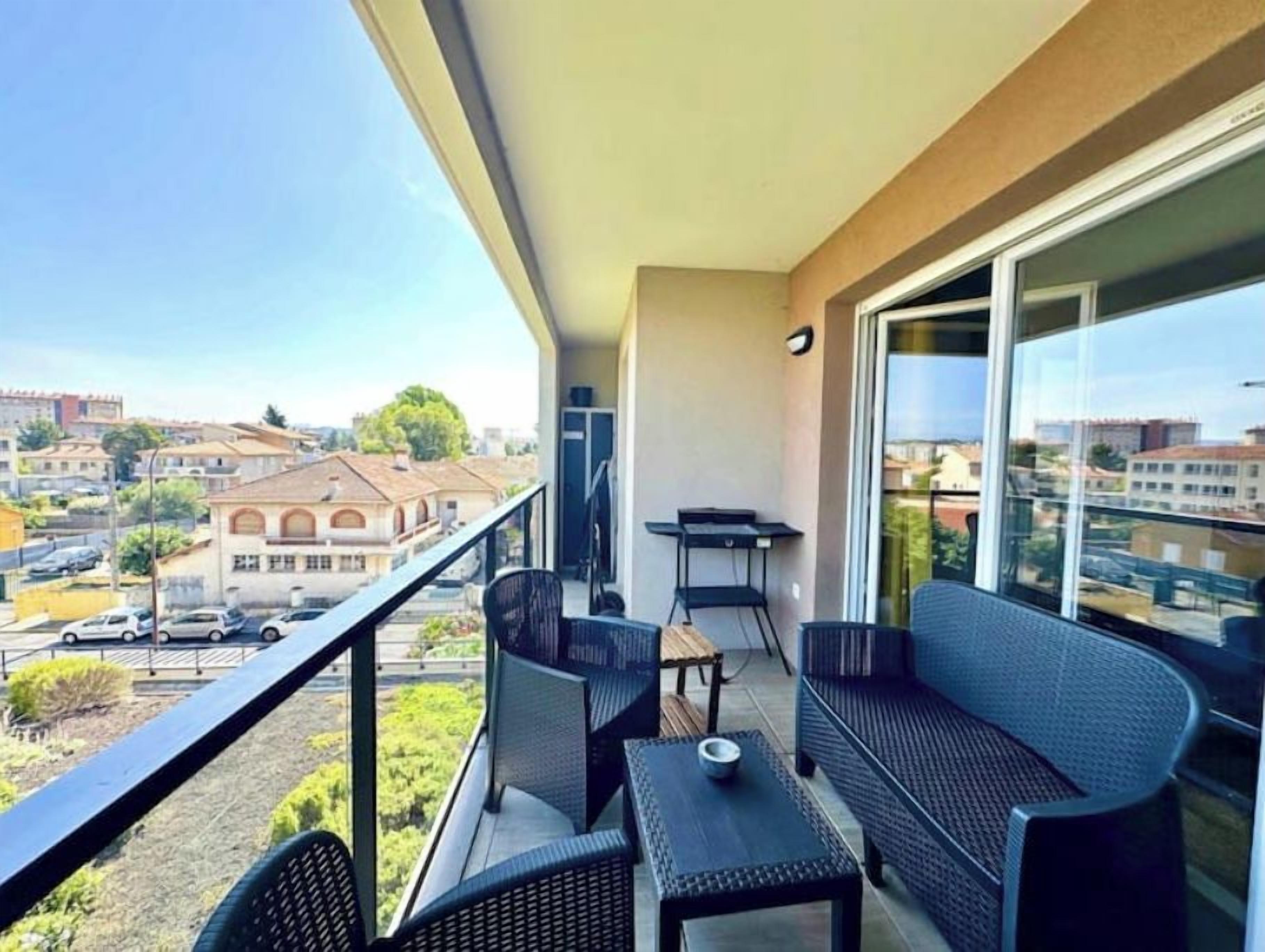 A balcony with a table and chairs, a sofa, and a view of buildings and a street.