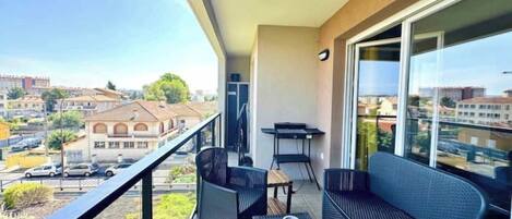 A balcony with a table and chairs, a sofa, and a view of buildings and a street.