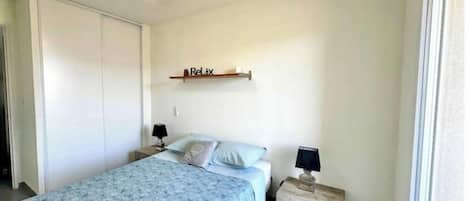 A bedroom with a bed, bedside tables, a ceiling fan, a shelf with a 'Relax' sign, and a window.