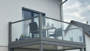 A balcony with a glass railing, a chair, and a table.