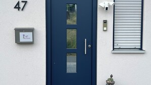A dark blue door with a glass panel, a mailbox with a house number, a welcome mat, and a window with blinds.