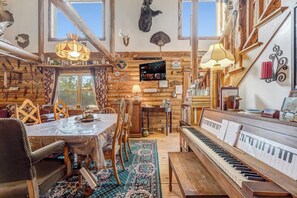 Un intérieur rustique avec une table à manger en bois, des chaises, un piano et un téléviseur.