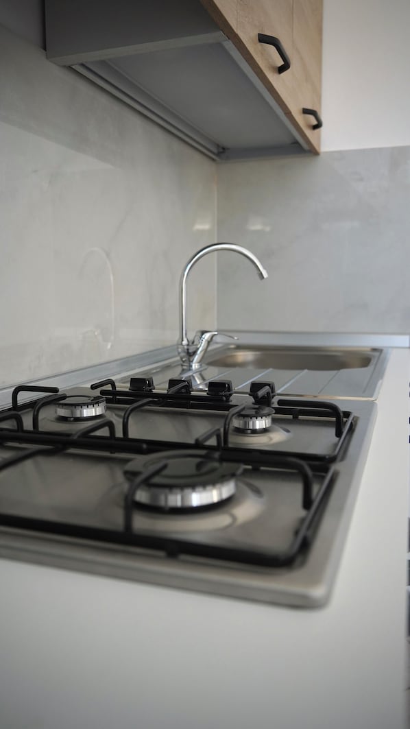 A kitchen with a white stove, four burners, a stainless steel faucet, and a wooden cabinet above the sink.