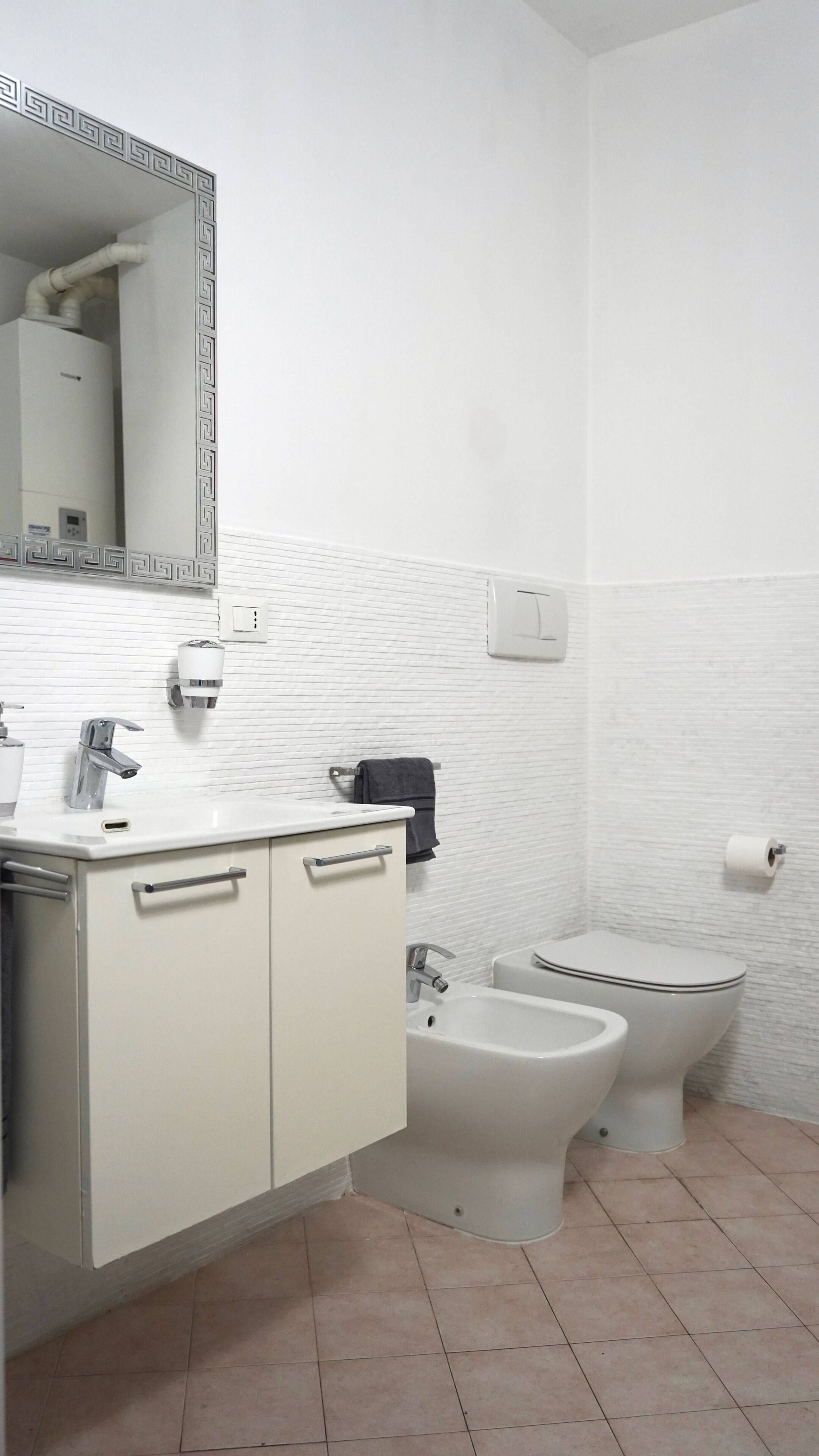 Une salle de bain avec un lavabo blanc, un miroir, des toilettes, un bidet et un porte-serviettes.