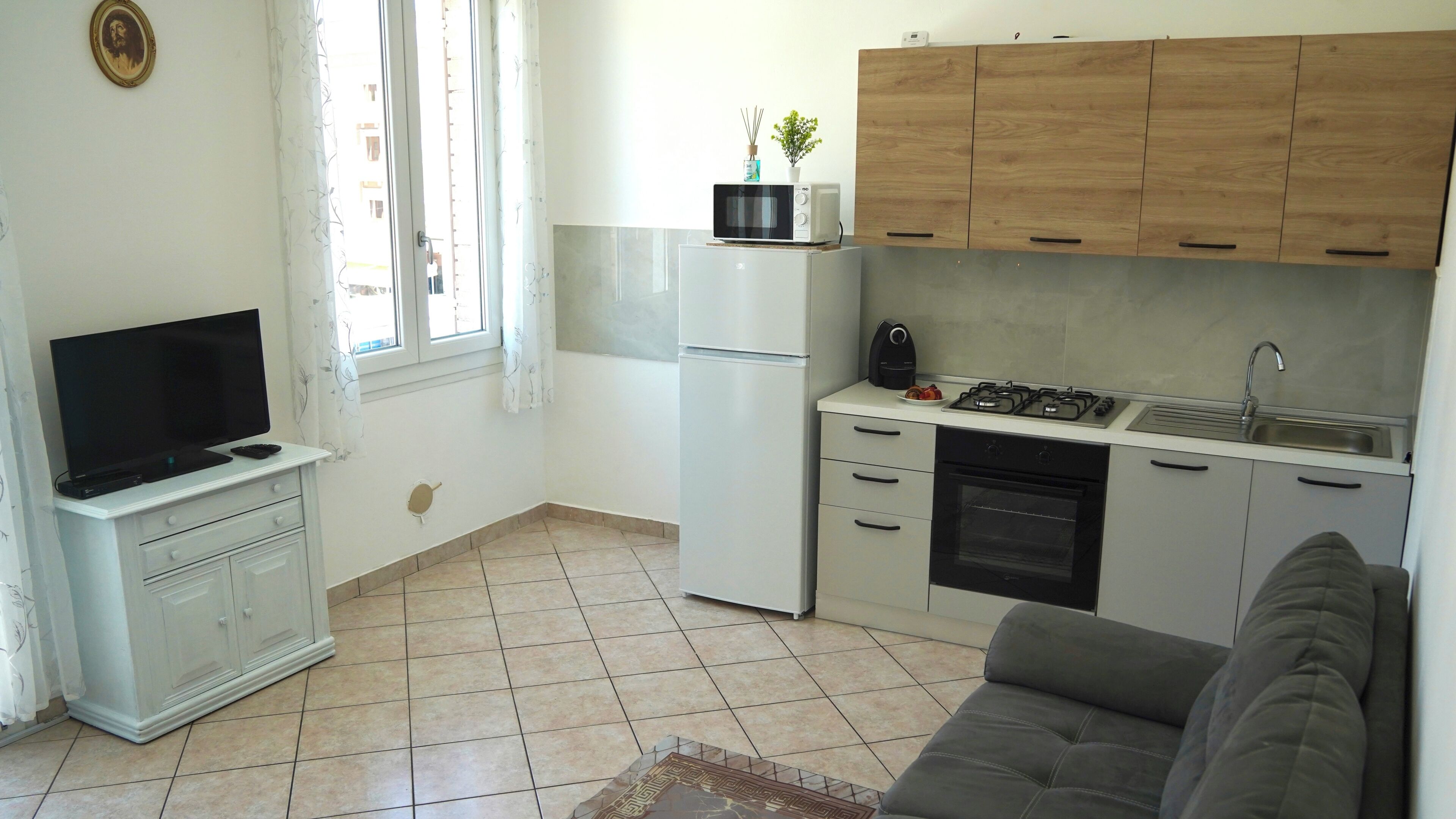 A compact living space with a kitchenette, a flat-screen TV, a sofa, and a window with curtains.