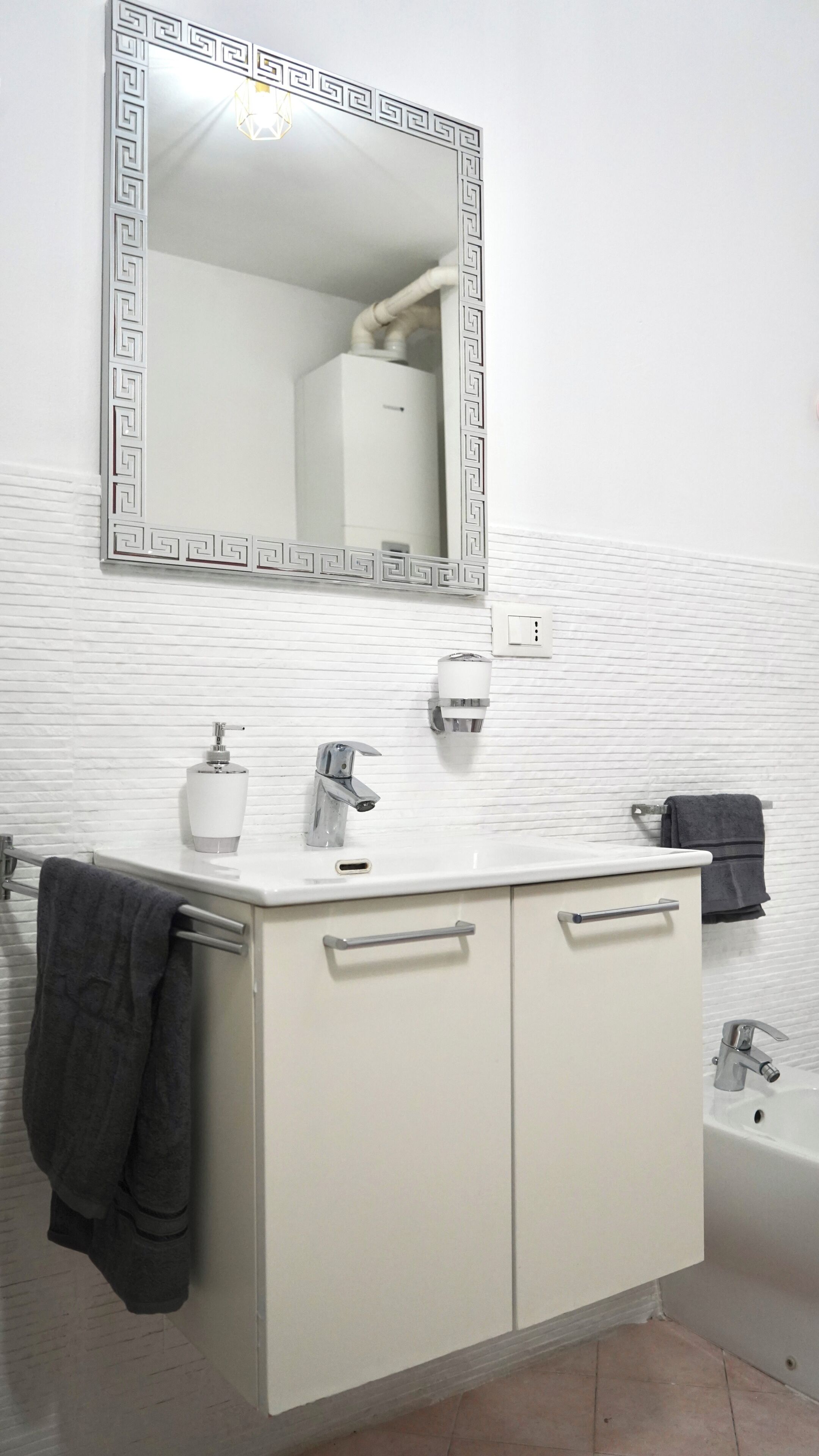 Un baño con un tocador blanco, un espejo con marco decorativo, un perchero y una bañera.