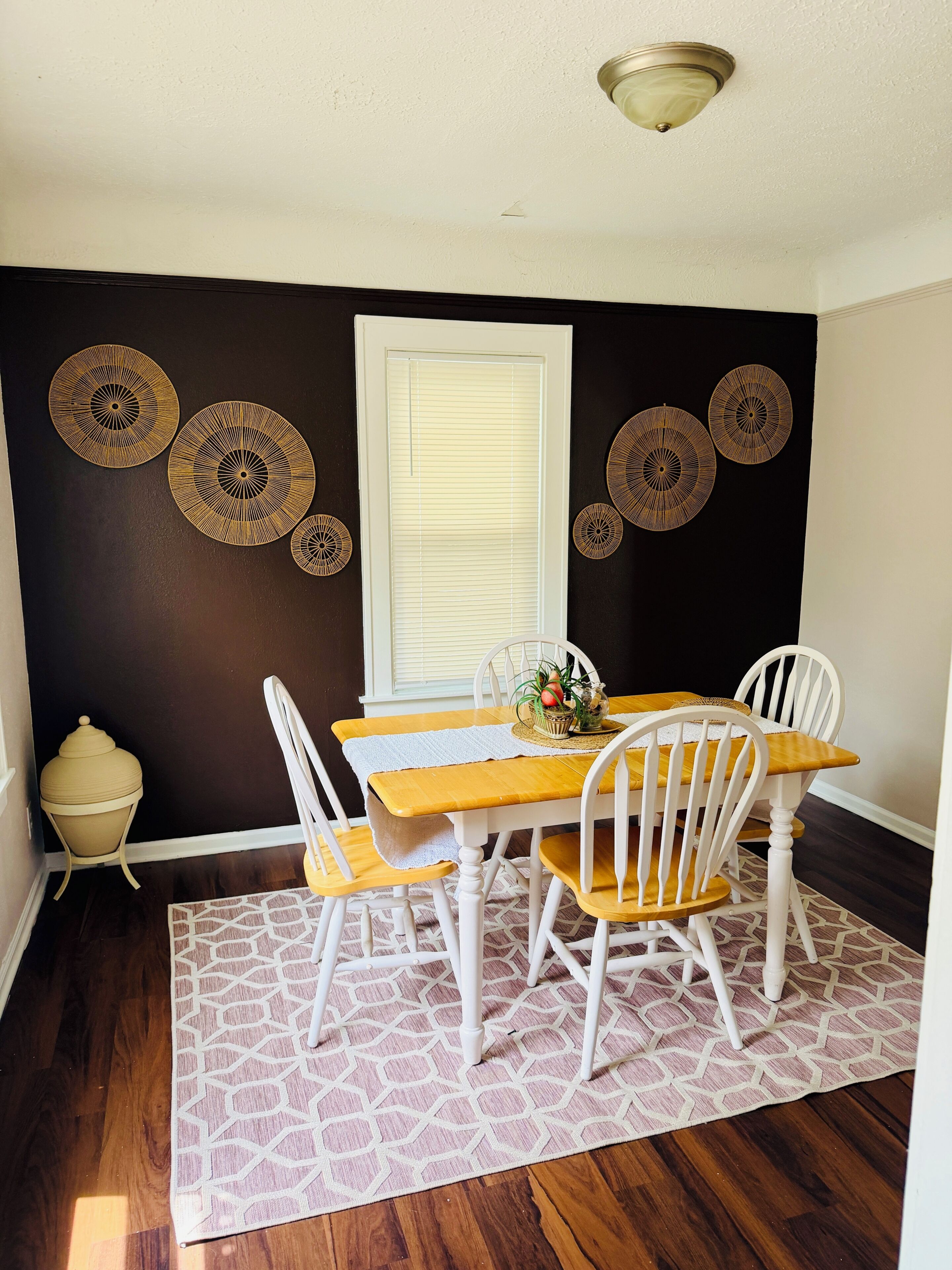 Un espace repas comprenant une table en bois, des chaises blanches, un tapis à motifs et des œuvres d’art décoratives accrochées au mur.
