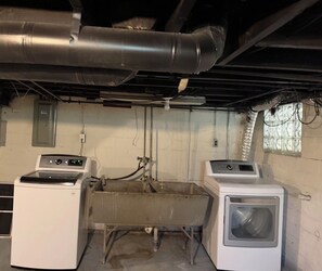 A laundry room with two washing machines, a large sink, and visible ductwork.