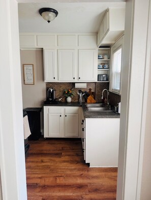 A kitchen with white cabinets, a black countertop, and a wooden floor.