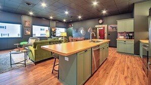 A compact kitchen with a central island, a dining area with a green sofa, and a view of the outside through large windows.
