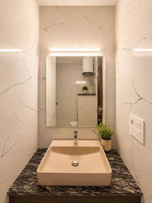 Une salle de bain avec un mur en marbre, un lavabo avec un robinet, un miroir et une plante en pot.