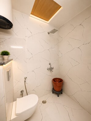 Une salle de bain avec un mur en marbre blanc, un plafond en bois, une douche, des toilettes et une petite plante en pot.