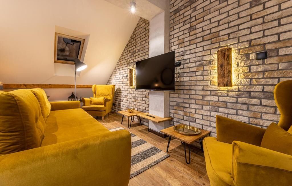 A modern living room with a brick wall, a flat-screen TV, and yellow furniture.