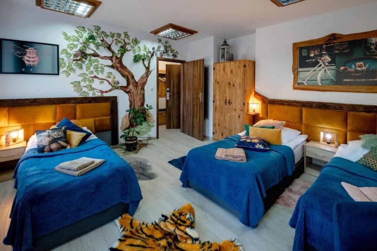 A hotel room with two beds, a large tree mural, a wooden wardrobe, and a painting on the wall.