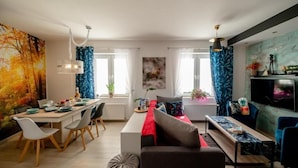 Un salon moderne avec un canapé, une table à manger et des chaises, ainsi qu’un téléviseur.