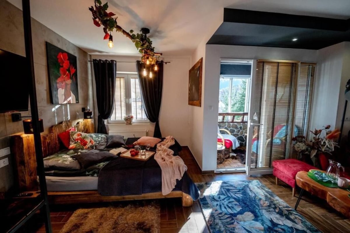 A bedroom with a bed, a window, a door, and a view of the outside.