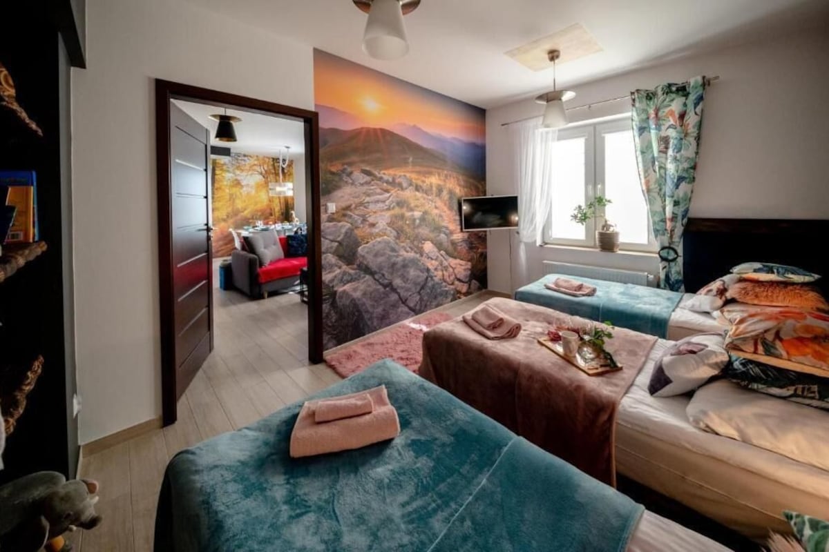 A hotel room with a bed, two sofas, a TV, and a painting of a landscape.