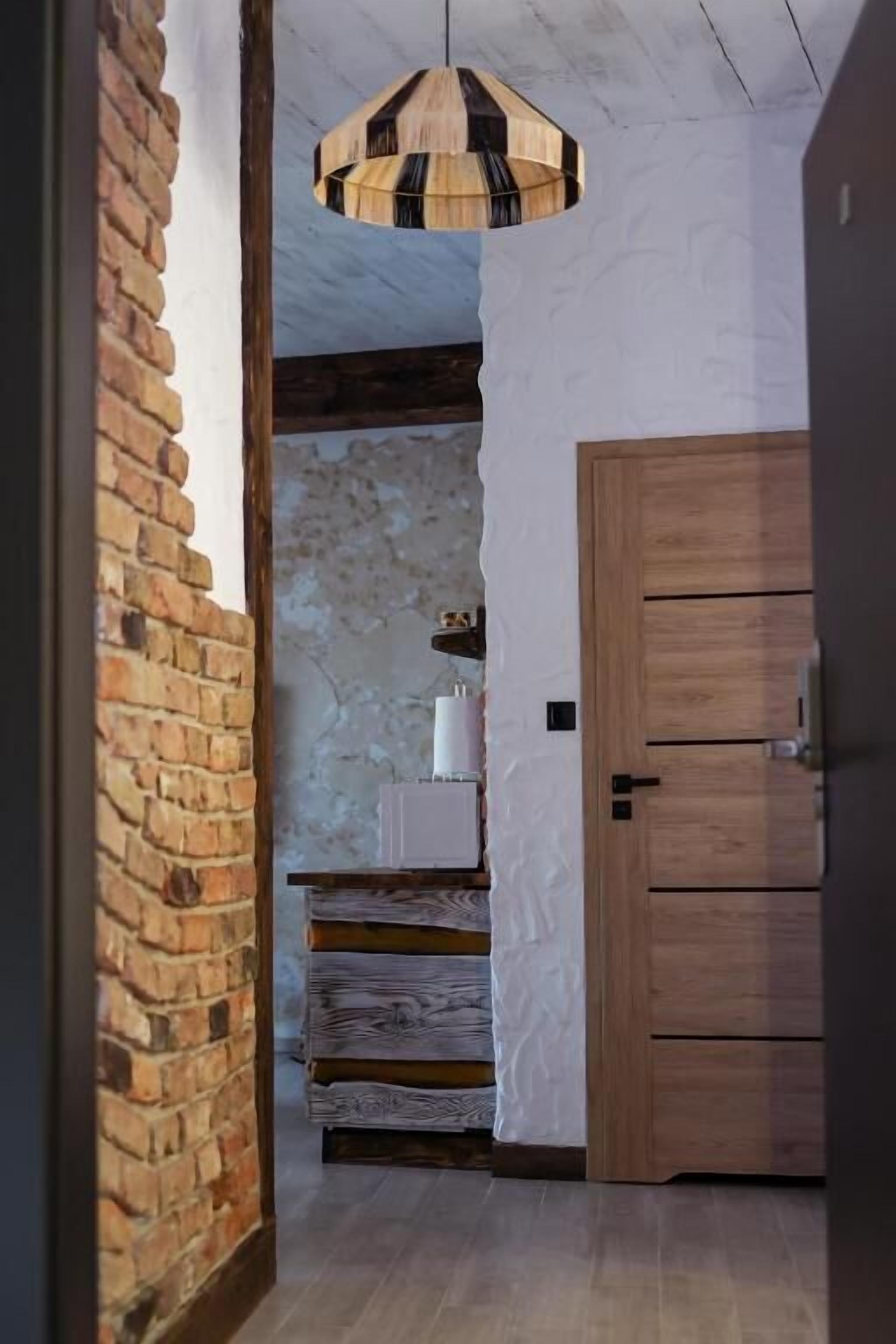 A hallway with a wooden door, a brick wall, and a ceiling light fixture.