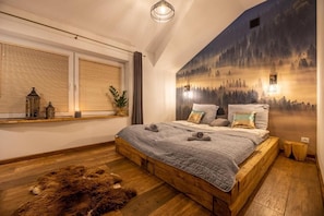 A bedroom with a wooden bed, a fur rug, a window with blinds, and a forest mural on the wall.