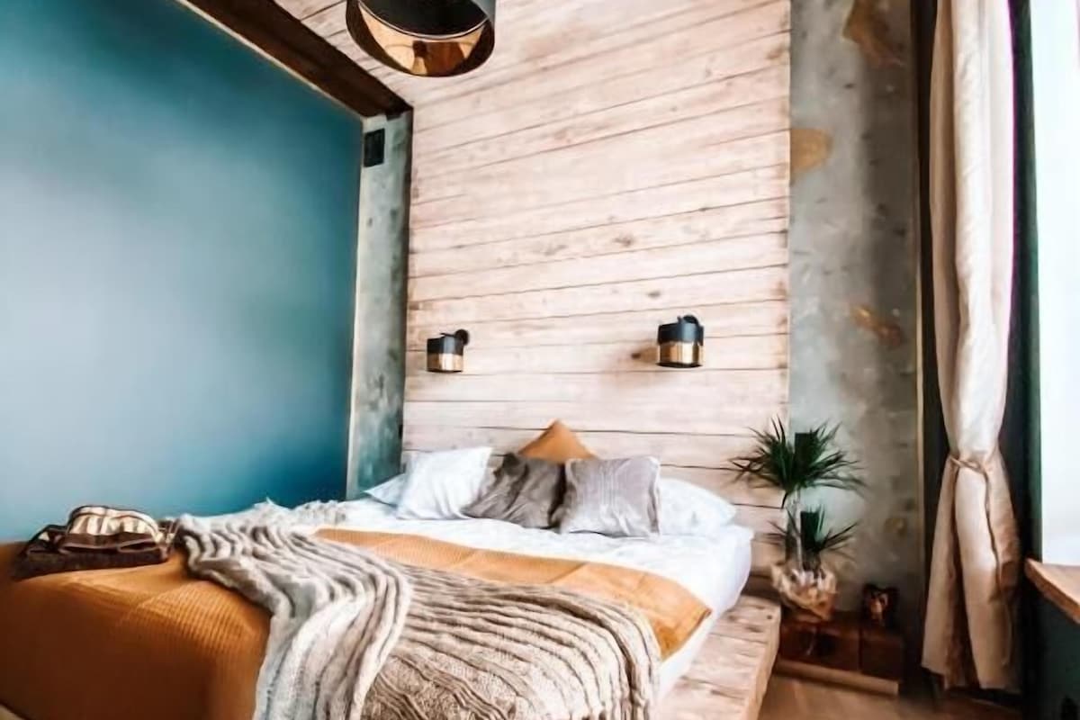 A room with a wooden bed, a hanging light fixture, a small plant, and a fur rug.