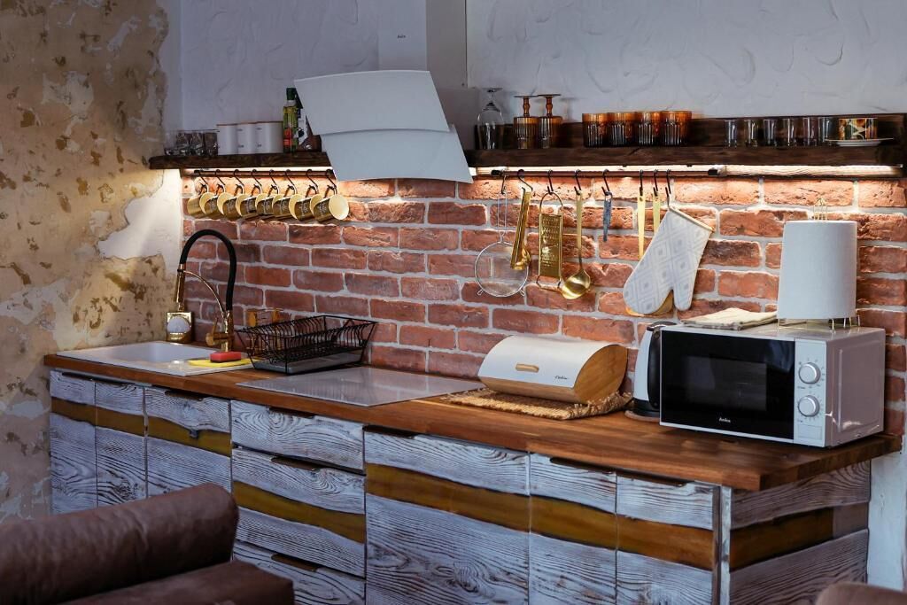A kitchen with a brick wall, wooden cabinets, a microwave, and hanging utensils.