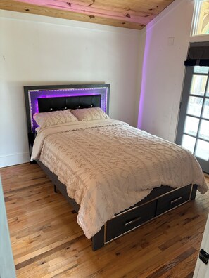 Ein Schlafzimmer mit Bett, Holzboden, einem Kopfteil mit LED-Beleuchtung und einem Fenster.