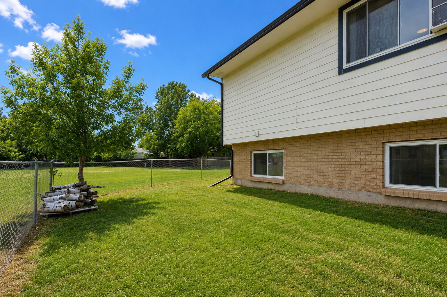 A residential building with a brick foundation and white siding, a fenced yard, and a tree.