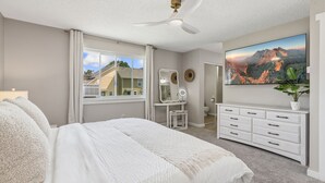 A bedroom with a bed, a vanity with a mirror, a dresser, a ceiling fan, and a large window. - Windsor Wanderer Walk to Parks, Pool, Downtown (Windsor)
