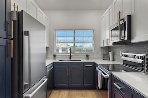 A modern kitchen with a stainless steel refrigerator, a microwave, and an oven. There is a window with blinds, and a sink with a faucet. - Near Stadiums | Ultimate Sports Getaway (Scottsdale)