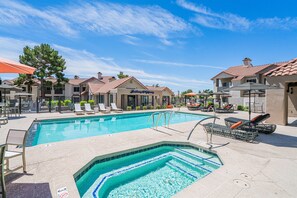 Une piscine dotée de chaises longues et d’un jacuzzi, entourée de maisons, avec un ciel dégagé.