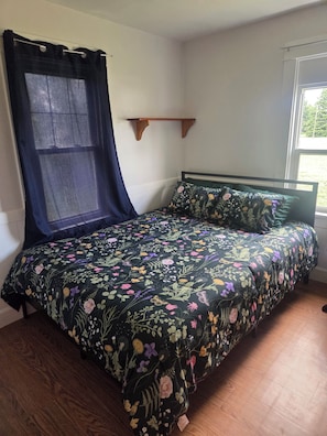 A bedroom with a bed, a window with a curtain, and a wooden shelf.