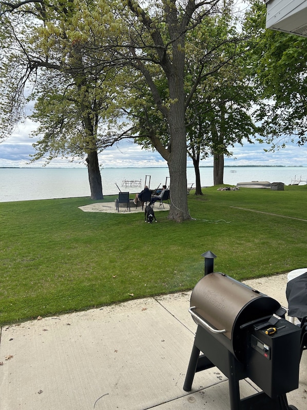 A grassy area with a lake view, a barbecue grill, and a couple of chairs.