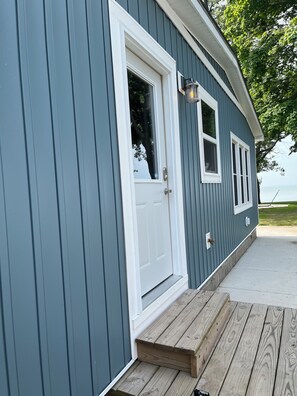 A blue building with a white door and windows, a wooden deck, and a view of the water.