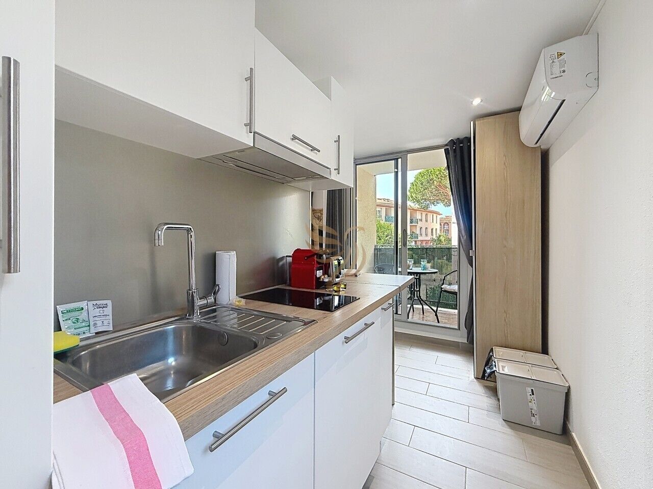 A compact kitchen with a sink, stove, and cabinets, leading to a balcony with a view.
