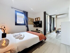 Ein modernes Hotelzimmer mit Bett, Schreibtisch, Flachbildfernseher, einer Weltkarte an der Wand und Blick auf das angrenzende Zimmer.