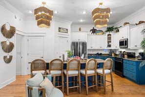 A kitchen with white cabinets, a blue island, and wooden chairs. - Pool • 1-Min Beach Walk • Game Room • Sleeps 14 (Panama City)