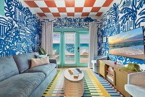 A living room with a sofa, coffee table, and bookshelf, a patterned floor, and a view through a door. - Pool • 1-Min Beach Walk • Game Room • Sleeps 14 (Panama City)