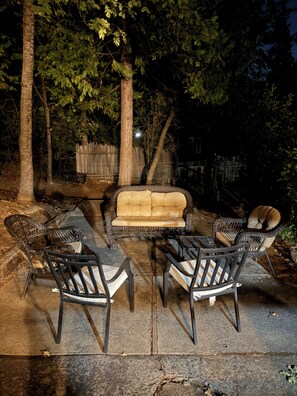 Un espace extérieur aménagé avec un canapé et des fauteuils, entouré d’arbres et d’une clôture en bois.