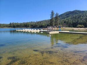 Un lac aux eaux limpides, avec un quai et un petit bâtiment, le tout entouré de collines boisées.