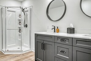 A modern bathroom with a glass shower enclosure, a sink with a mirror, and grey cabinetry. - Thalia Bright Designer Home 12 Min To Falls (Thorold)
